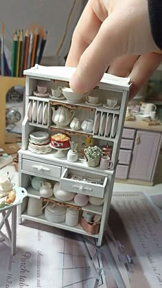 a miniature model of a kitchen with pots and pans on the shelves, in someone's hand