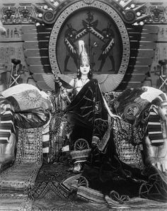 an old black and white photo of a woman sitting in front of a large statue