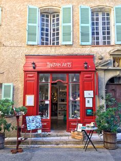 a red store front with green shutters on it's windows and plants outside