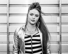 a woman with long hair and piercings standing in front of a garage door wearing a jacket