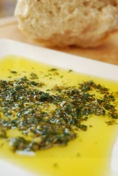 a white plate topped with green food next to a loaf of bread on top of a wooden table