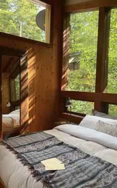 a bed sitting in a bedroom next to two windows with trees outside the window sill