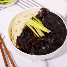 a white bowl filled with noodles and meat on top of a table next to chopsticks