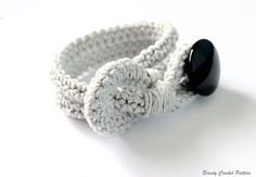 a crocheted bracelet with a black button on it's end, sitting on a white surface