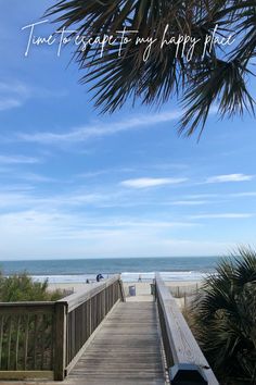 a wooden walkway leading to the beach with palm trees in the foreground and an ocean view