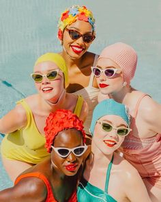 four women in bathing suits and sun glasses pose for a photo by the swimming pool