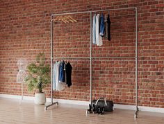 an empty room with clothes hanging on racks and a potted plant in the corner