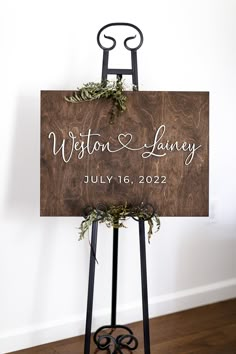 a wooden sign sitting on top of a metal easel with greenery in it