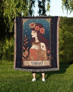 a woman standing in the grass holding up a tapestry with an image of a woman on it