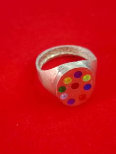 a silver ring with multicolored dots on it sitting on a red tablecloth