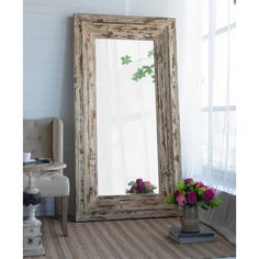 a large mirror sitting on top of a wooden floor next to a vase filled with flowers