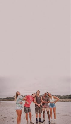 four people standing on the beach with a kite in the sky