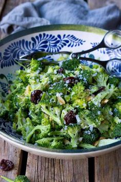 a bowl filled with broccoli and cranberries on top of a wooden table