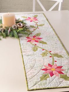 the table runner is decorated with poinsettis and greenery, along with a lit candle