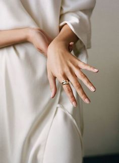 a woman in white dress with her hand on the back of her dress, wearing a gold ring