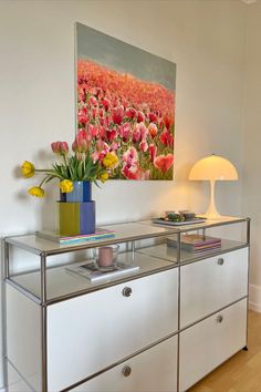 a painting is hanging on the wall above a glass table with flowers in vases