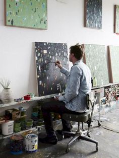 a man sitting at a desk painting on canvases