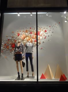 two mannequins are standing in front of a display window with geometric shapes