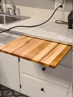 a wooden cutting board sitting on top of a kitchen counter next to a metal sink