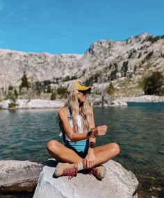 a woman sitting on top of a rock near the water