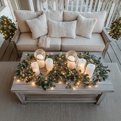 candles are lit on a coffee table in front of a couch with greenery around it