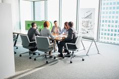 group of business people sitting around a conference table in an office setting with large windows