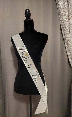 "This bridal sash is made with 3 inch soft satin and has \"Bride to Be\" in black letters.  Complimented with a unique gold heart with a cluster of hearts inside. The Sash is 72 inches in length and comes with a crystal pin to secure the Sash in place. This sash is perfect for a bridal shower, wedding party, or a bachelorette party." Bride Sash Bachelorette, Sash Bachelorette, Bride Sash, Bridal Shower Sash, Gold Sash, Bachelorette Sash, Bride To Be Sash, Wedding Sash Belt, Wedding Sash