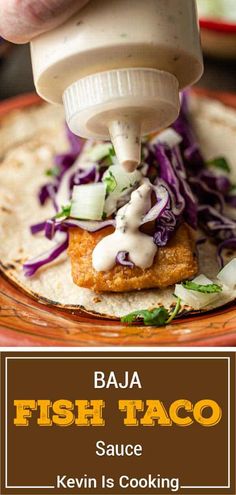 a person pouring sauce on fish taco in a tortilla with cole slaw