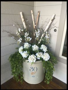 a white bucket filled with lots of flowers on top of a wooden floor next to a door