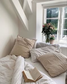 an unmade bed with white sheets, pillows and a book on the end table