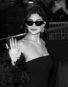 black and white photo of a woman in sunglasses holding her hand up to the camera