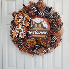 a welcome halloween wreath hanging on a door with an orange and black cat bow around it