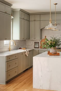 a kitchen with marble counter tops and wooden flooring is pictured in this image, there are two pendant lights hanging over the island