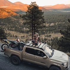 two people sitting on the back of a truck with their bikes in the bed and mountains in the background