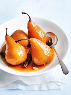 a white bowl filled with pears on top of a table next to a spoon