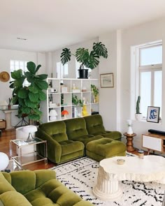 a living room filled with green couches next to a white table and potted plants