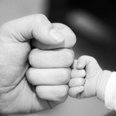 a black and white photo of a baby holding the hand of an adult's hand