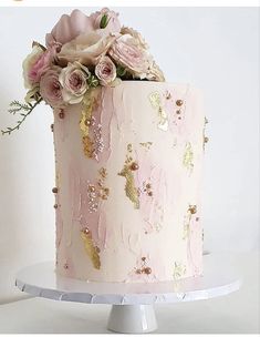 a pink and gold wedding cake with flowers on the top is sitting on a white stand