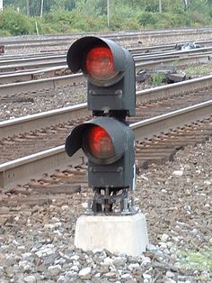 two traffic lights sitting on the side of train tracks next to each other, with trees in the background