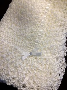 a white crocheted blanket with a bow on it's end laying on a table