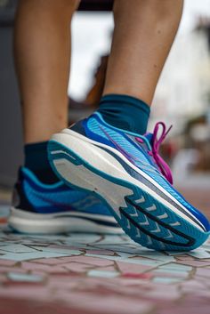 a person's feet with blue and pink running shoes on top of a tile floor