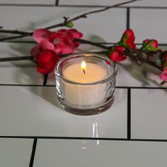 a lit candle sitting on top of a white tile floor next to pink and red flowers