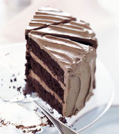 a slice of chocolate cake with frosting on a white plate and green border around it