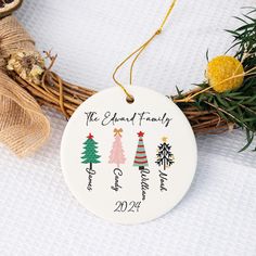 a personalized ornament with christmas trees on it next to a wreath and twine