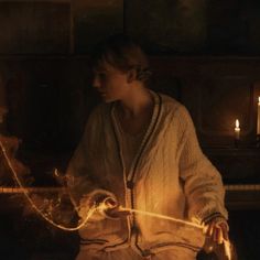 a woman sitting in front of a piano holding a string with two candles behind her