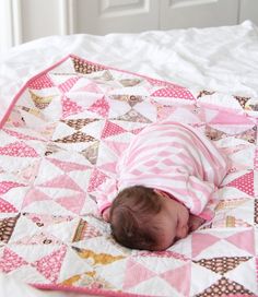 a baby sleeping on top of a pink and white quilt