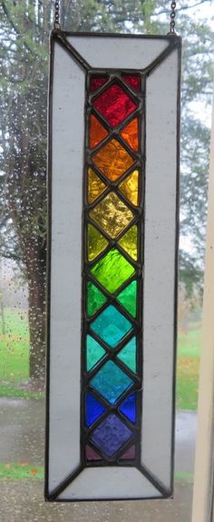 a colorful stained glass window hanging from a chain in front of a window sill