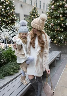 two girls in winter clothes and hats are walking down the street with christmas trees behind them