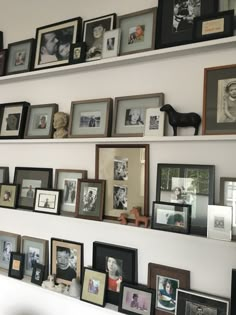 a wall filled with lots of framed pictures next to a shelf covered in photos and frames