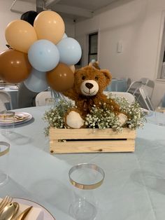 a brown teddy bear sitting on top of a wooden box filled with flowers and balloons